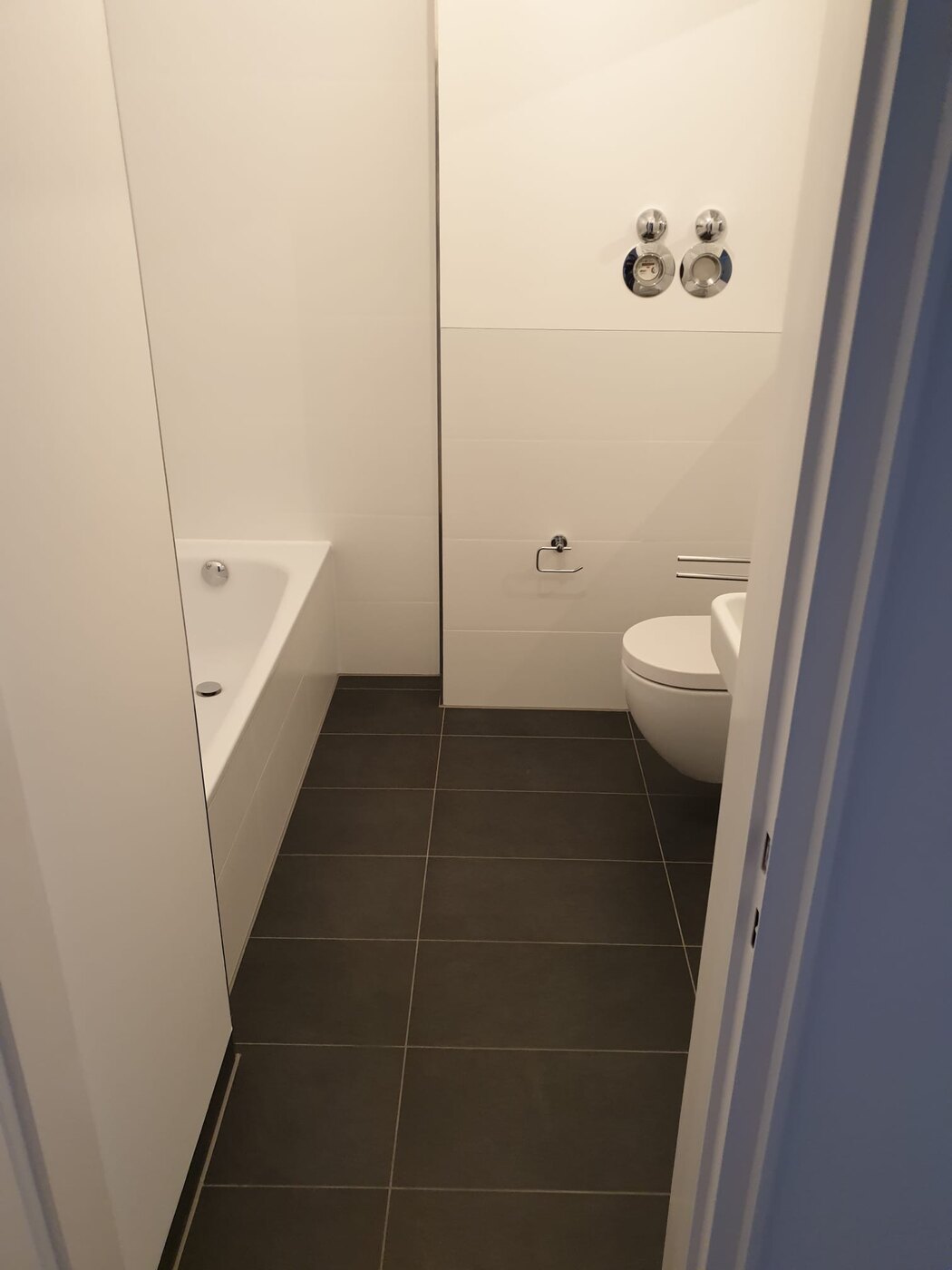 Badezimmer mit Badewanne, Wand-WC und dunklen Bodenfliesen